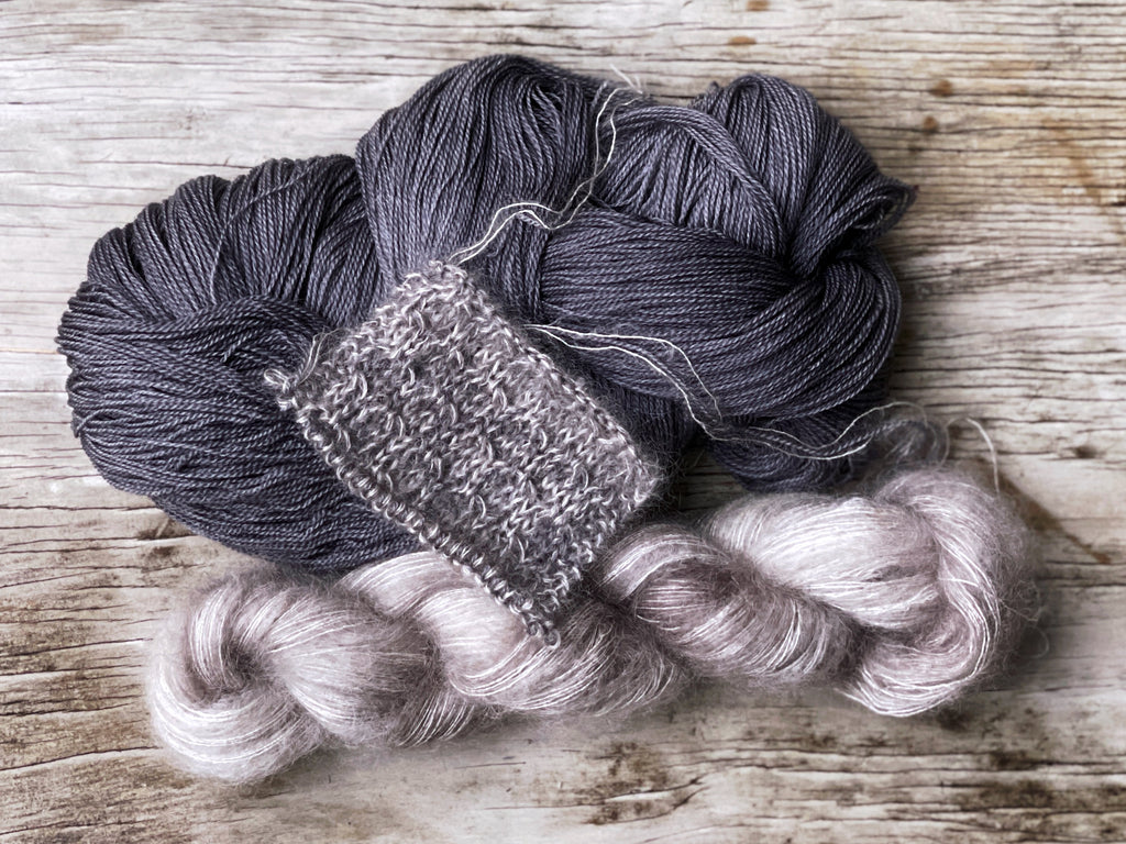 a twisted skein of bare, off white, very fine mohair and merino yarn sits on a weathered piece of wood.